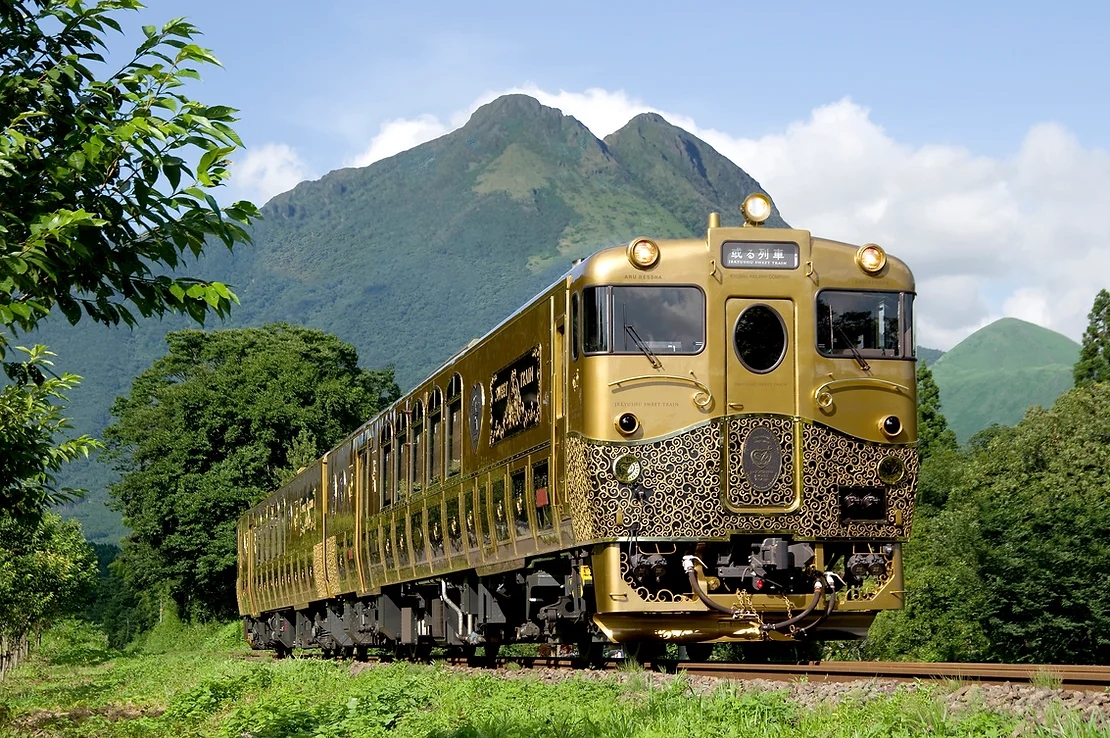 Gold with black swirling patterns on the exterior luxurious train traveling past mountains in the Kyushu Japanese countryside